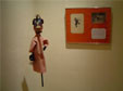 À direita, boneco da peça Onça e o Macaco (macaco), ao fundo moldura com desenho estudos sobre a peça.
<br/>
Local: Museu Alfredo Andersen - Rua Mateus Leme, 336 - Centro - Horário: 2ºa 6º feira: 9h00 às 18h00 - Sábados e Domingos das 10h00 às 16h00