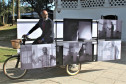 Obra "A Dúvida da Verdade" de Sérgio Adriano H., composta por uma bicicleta triciclo com caixa baú, estrutura metálica modular e 12 fotografias impressas sobre PVC.