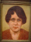 Retrata figura feminina em posição frontal. Cabelos curtos e castanhos, olhos também castanhos, olheiras bem marcadas, sobrancelhas afiladas, lábios pequenos semicerrados. Tez clara levemente rosada. Traja roupa vermelha. Fundo claro e amarelado.